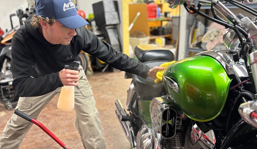 Technician detailing a green motorcycle on a lift