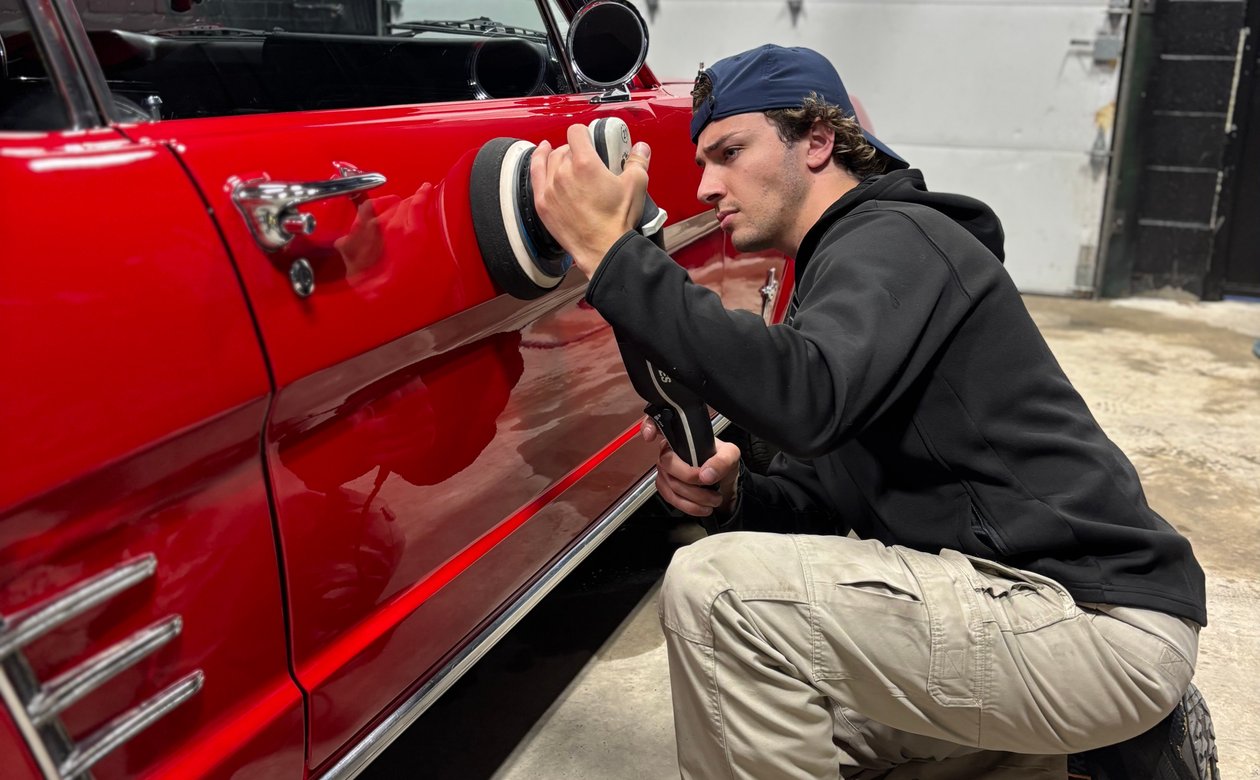 Technician machine polishing the door of a classic red car