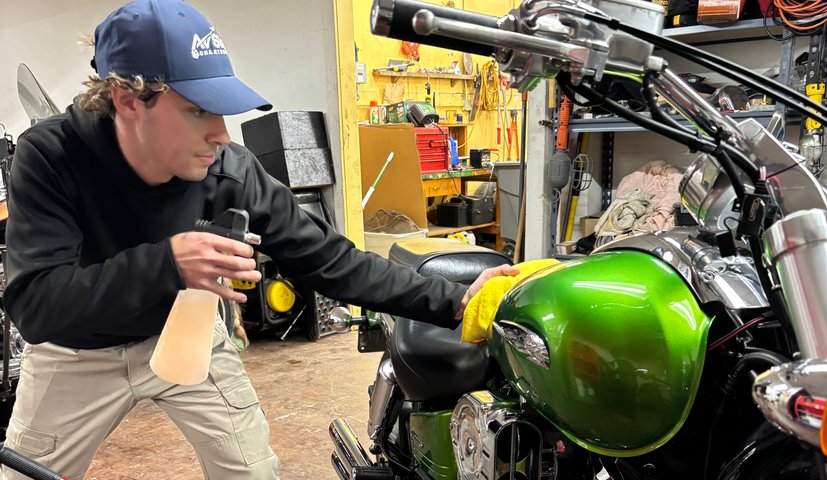 Technician detailing a green motorcycle on a lift